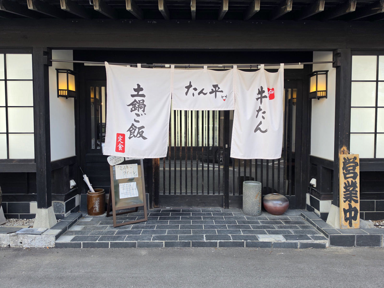 白壁と黒い柱の店先。「土鍋ご飯」「たん平」「牛たん」の三枚の暖簾、両脇に行灯、右に「営業中」の木札。