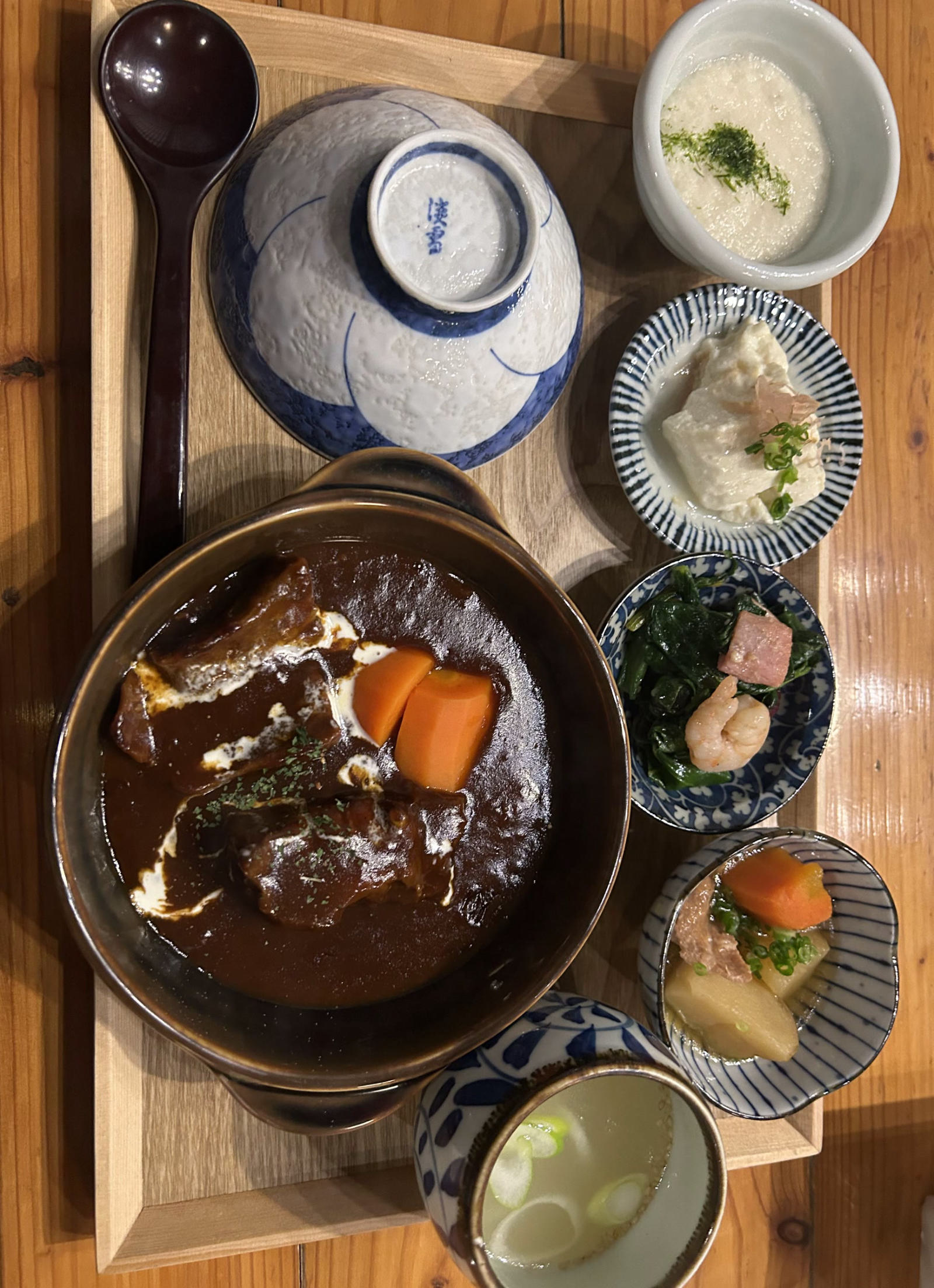 牛たんシチューの膳を真上から。土鍋のシチューに人参と生クリーム、伏せた染付の飯碗、とろろ、小鉢三品、スープ。