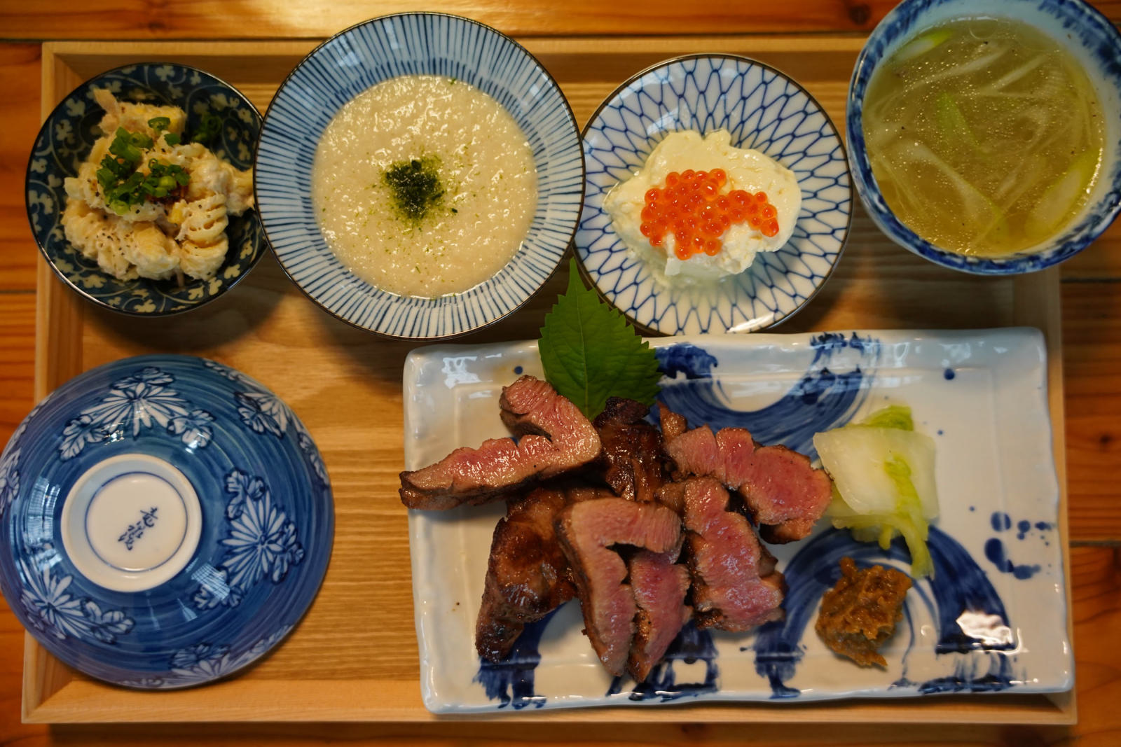 真上から見た膳。染付の皿に中がほんのり赤い牛たん焼きと大葉、白菜の漬物、南蛮味噌。とろろ、いくら豆腐、スープ、小鉢。