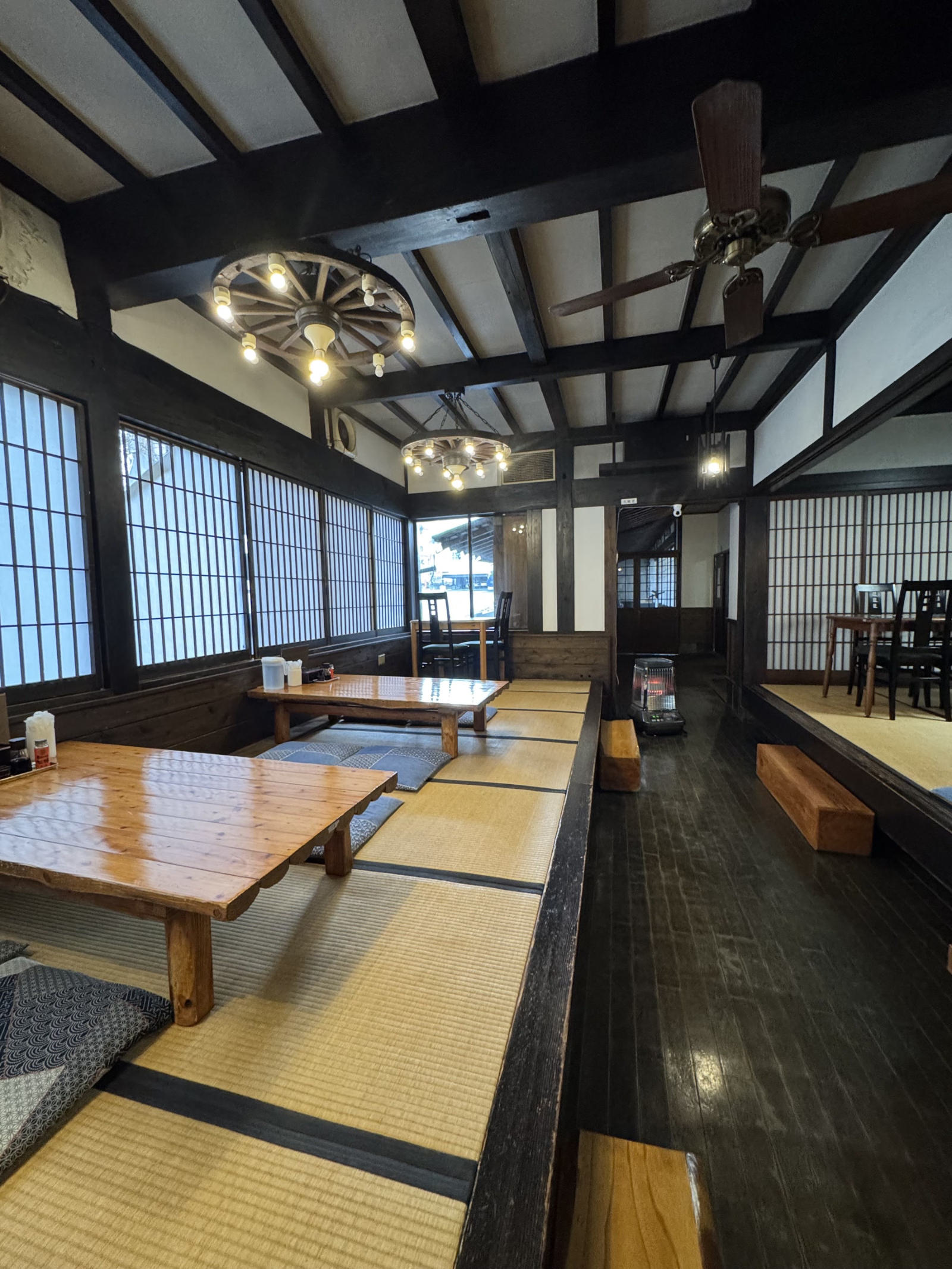 細長い店内。黒い板の通路の左に座卓を並べた小上がり、右に畳敷きのテーブル席。天井に車輪の照明とシーリングファン。