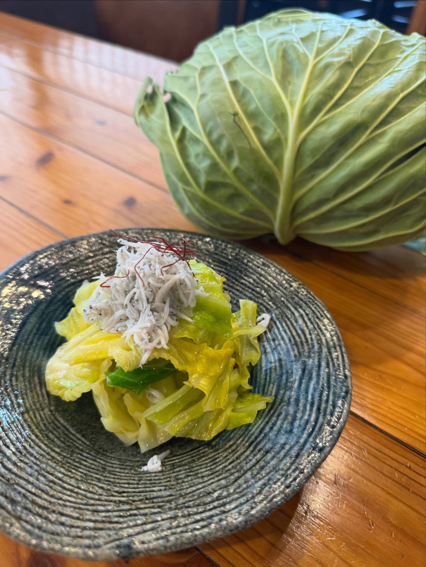 しらすと糸唐辛子をのせたキャベツの炒め物。奥に丸ごとのキャベツ。